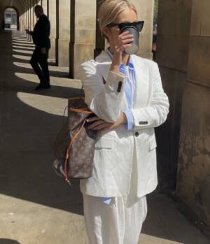 Blogger wearing a white suit with blue shirt and a Louis Vuitton Monogram Neverfull bag on one shoulder.