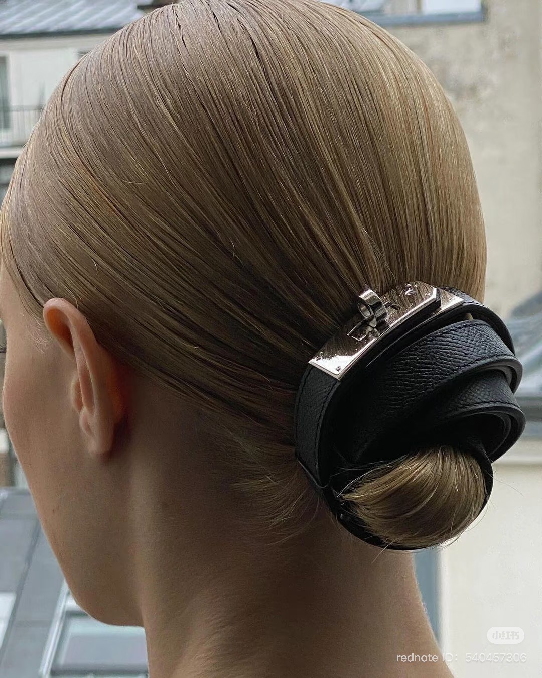 hermes kelly belt in black with silver hardware used to hold together a bun style in woman's hair
