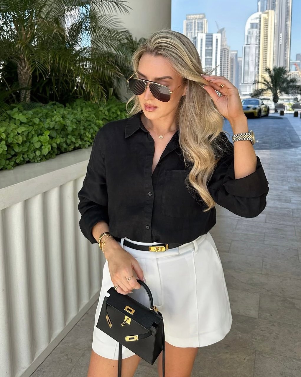 woman wearing hermes kelly belt in black with a black mini kelly with gold hardware