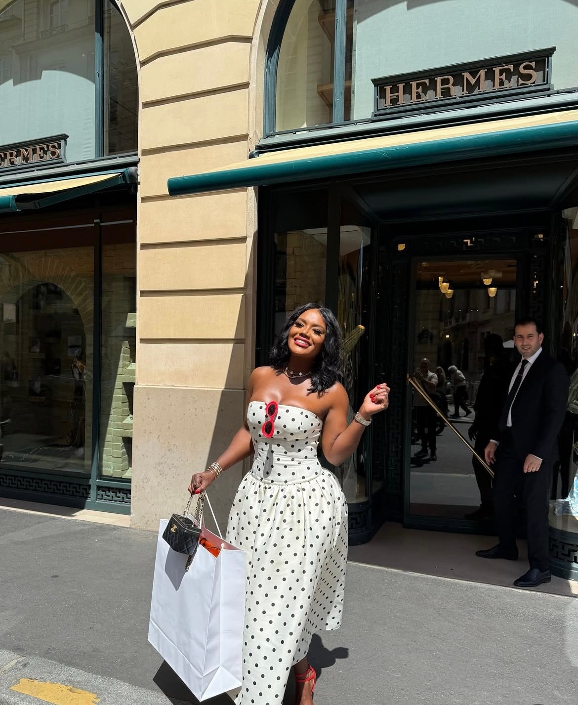 woman in polka dot dress in front of hermes fsh paris who just bought a birking bag from her leather appointment in paris at hermes.